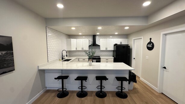 A modern kitchen with white cabinetry, a black refrigerator, and a central island with bar stools. - Y Mountain Modern (Provo)