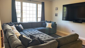 A living room with a sectional sofa, a flat-screen TV, and large windows with curtains. - Y Mountain Modern (Provo)