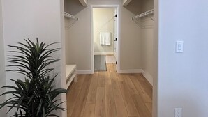 A hallway with wooden flooring and white walls, leading to a bathroom with a shower and a towel rack. - Y Mountain Modern (Provo)