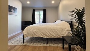 A bedroom with a bed, a small table, a potted plant, and a window with curtains. - Y Mountain Modern (Provo)