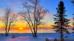 A snowy landscape with trees and a sunset over a body of water.