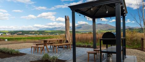 Un patio al aire libre con una parrilla, mesas de picnic y una pérgola.
