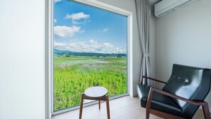 A room with a large window offering a view of a green field and distant mountains. - Yugen Retreats Furano (Kamifurano)
