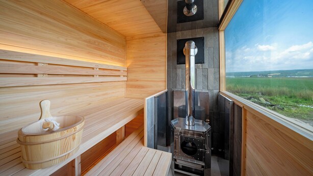 A sauna room with wooden benches, a stone wall, and a sauna stove. - Yugen Retreats Furano (Kamifurano)