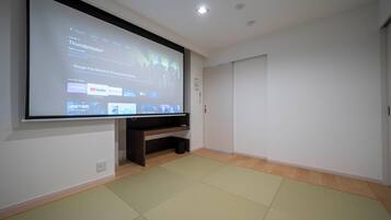 Una habitación con una televisión de pantalla grande de montaje en pared, un mueble de entretenimiento de madera oscura debajo y suelo de esteras de tatami.