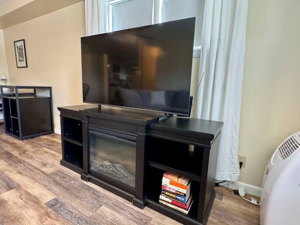 A living room with a large flat-screen TV, a fireplace, and a bookshelf with books.
