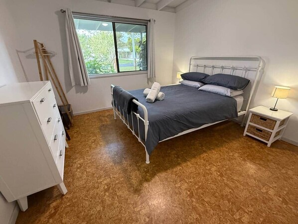 A bedroom with a bed, a dresser, a nightstand, and a window with curtains.