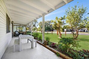 Une terrasse couverte avec une table et des chaises, une pelouse et une vue sur la rue.