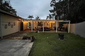 Een achtertuin met een overdekte patio, gazon en een huis met garage.