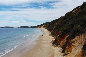 Une plage avec une rive sablonneuse et une falaise abrupte d’un côté.