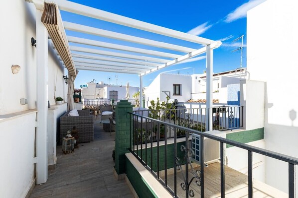 A covered outdoor balcony with wicker furniture, a grill, and a view of neighboring buildings. - Townhouse, Old Town, Nerja (Nerja)