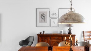 Een eetgedeelte met een houten tafel, stoelen, een kroonluchter en lijstwerken aan de muur.