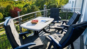 A balcony with a table and chairs, a basket of fruit, and a view of trees and a building. - Beautiful apartment for 4 people with WIFI, TV and terrace (Wolgast)