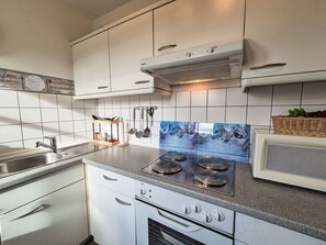 Una cocina moderna con armarios blancos, un lavamanos de acero inoxidable, una estufa integrada y un microondas.