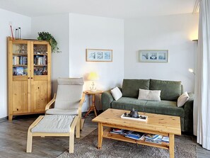 Un salon comprenant un meuble en bois, un canapé, un fauteuil, une table basse et deux tableaux accrochés au mur.
