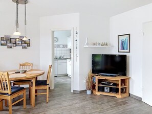 Ein modernes Wohnzimmer mit einem Holzespeisetisch, Stühlen, einem Flachbildfernseher auf einem Holzständer und einem Flur, der in eine Küche führt.