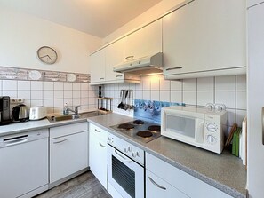 Una cocina moderna con armarios blancos, estufa, microondas y un reloj en la pared.