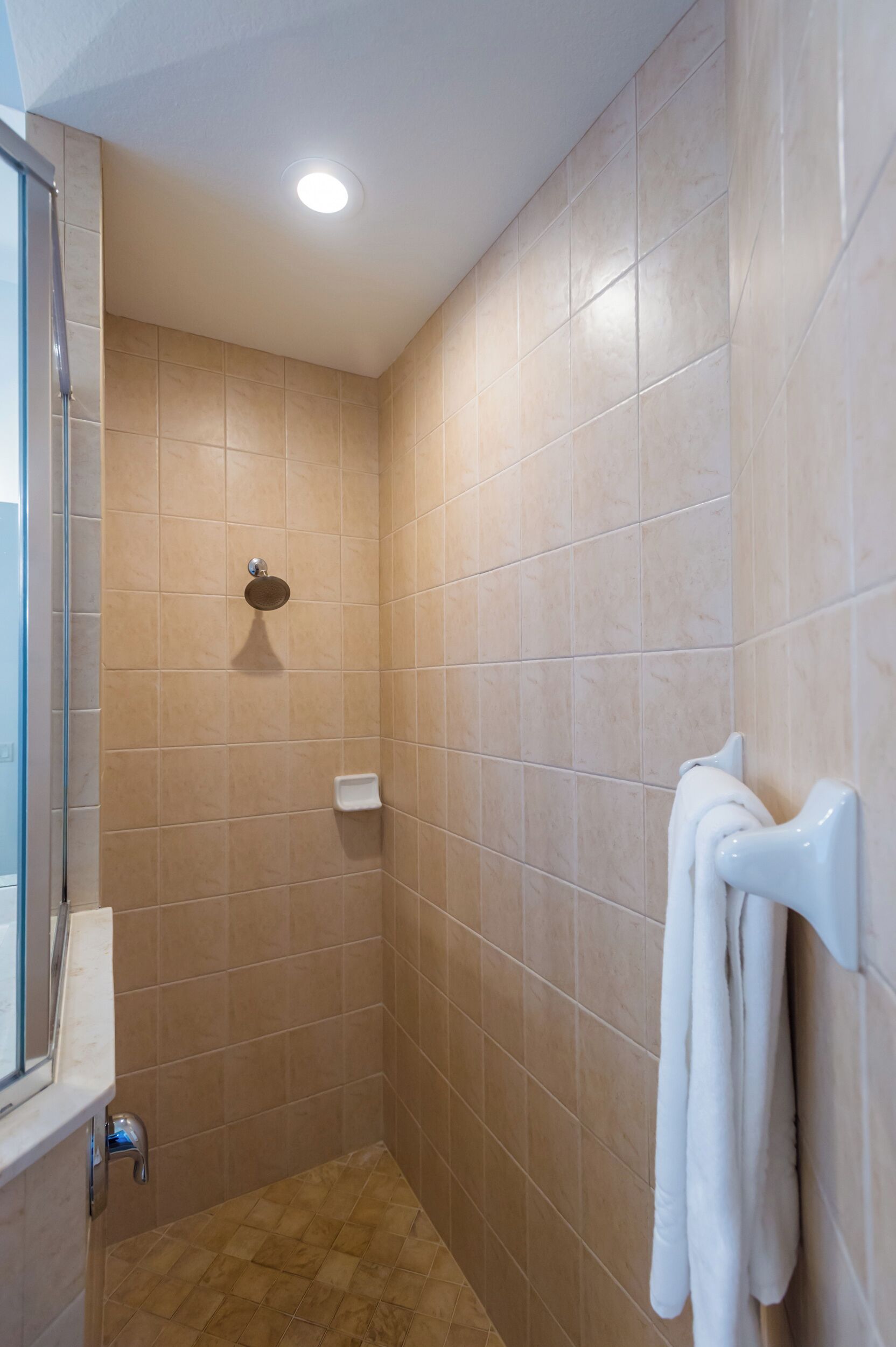 A bathroom with beige tiles, a glass shower enclosure, a white towel rack, and a handheld showerhead.