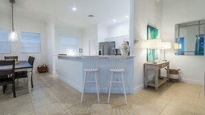 Una cocina moderna con armarios blancos, una isla central con taburetes de bar, un refrigerador y un espejo grande sobre la isla.