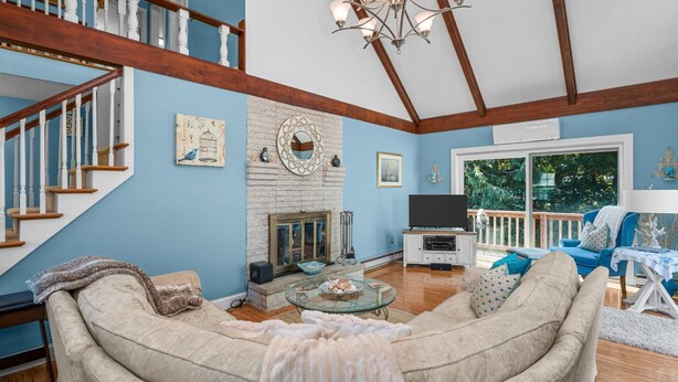 A living room with a staircase, a fireplace, a television, and a large window overlooking a deck. - Cape Cod Escape – 1 Mile to Beach, A/C & Grill (Centerville)