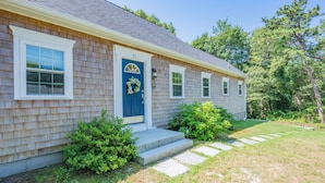 A single-story house with a blue front door, white-framed windows, and a small porch with steps leading to the door. - Cape Cod Escape – 1 Mile to Beach, A/C & Grill (Centerville)