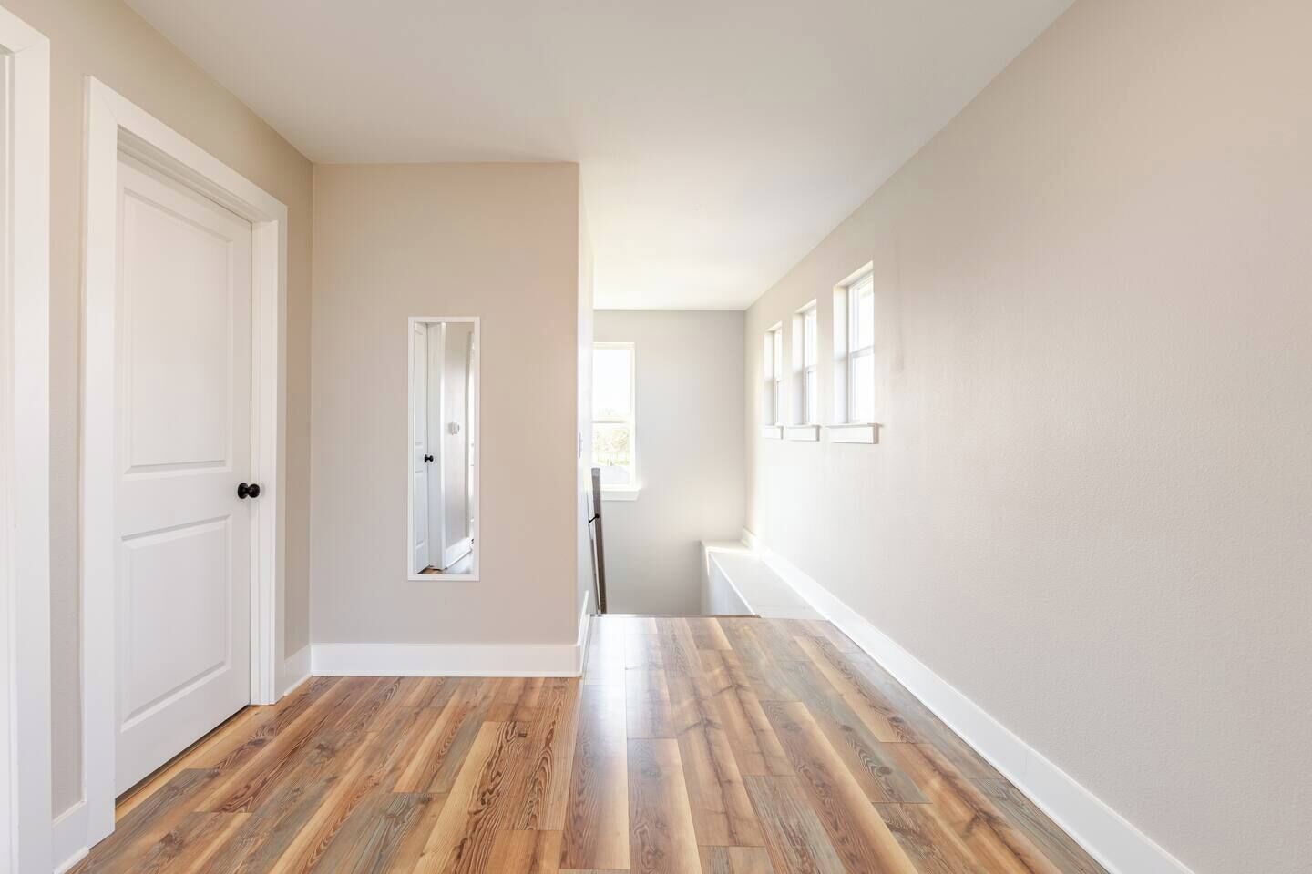 Un couloir avec un plancher en bois, des murs blancs et une porte sur le côté gauche.