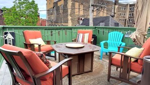 Une terrasse extérieure avec une table et des chaises, une clôture verte et des bâtiments en arrière-plan.