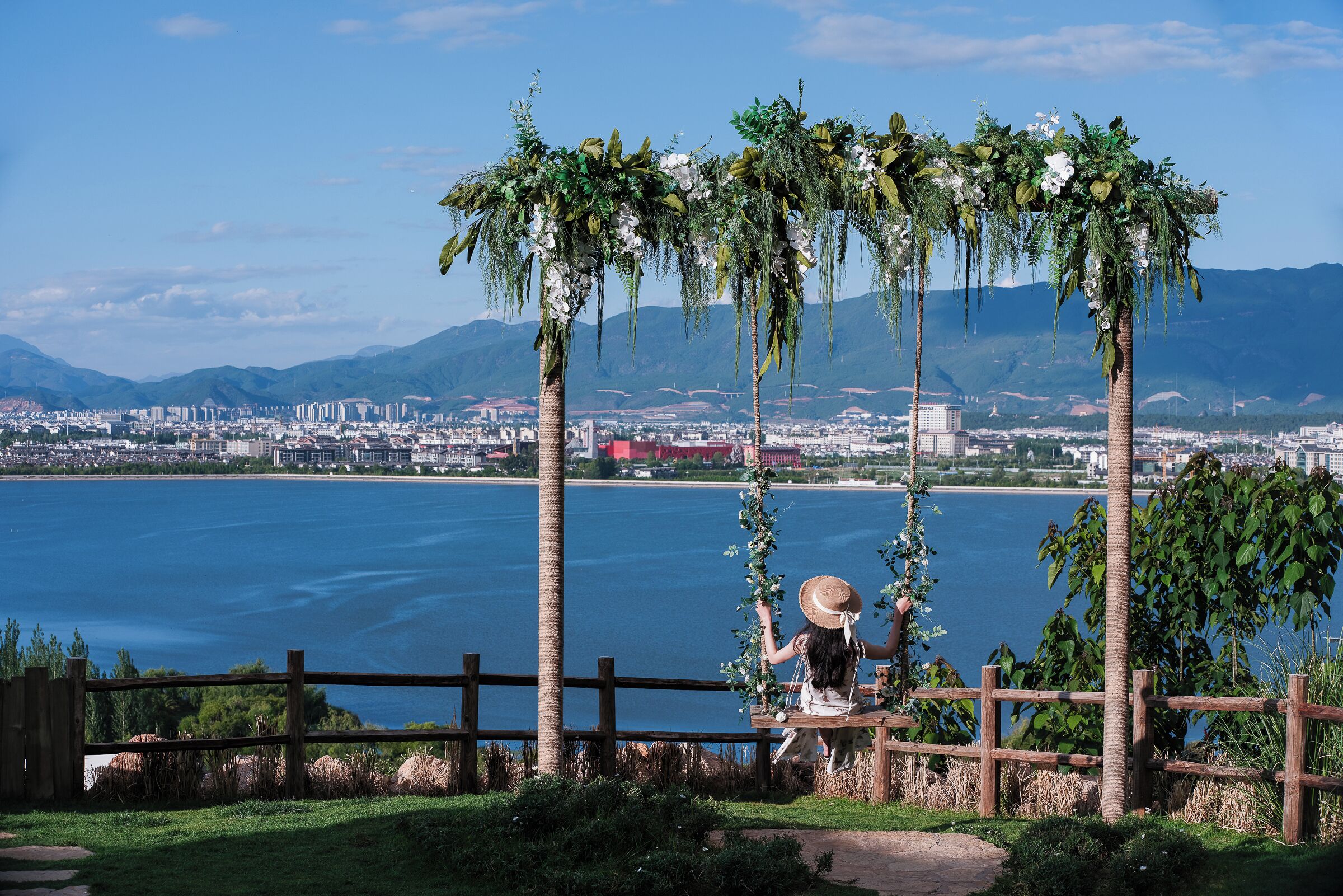 A view of a coastal city with a wooden fence, palm trees, and a person sitting on a bench.