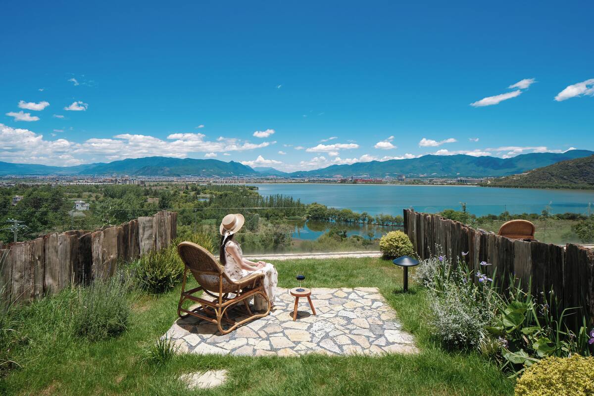 Un patio con una silla de mimbre y una pequeña mesa, con vistas a un lago y montañas.