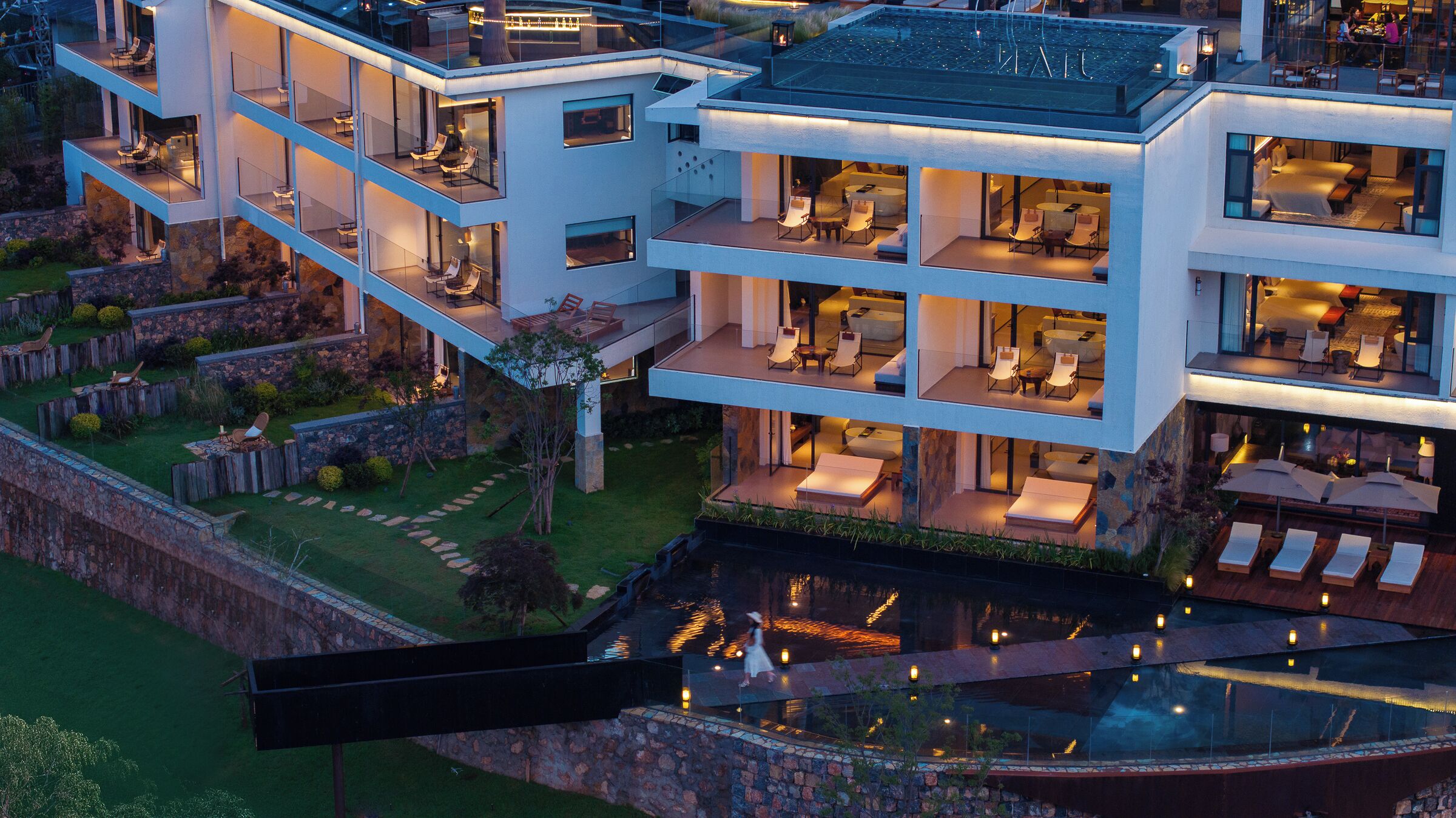 Un edificio moderno de varios pisos con zonas de estar al aire libre, una piscina y un muro de contención de piedra.