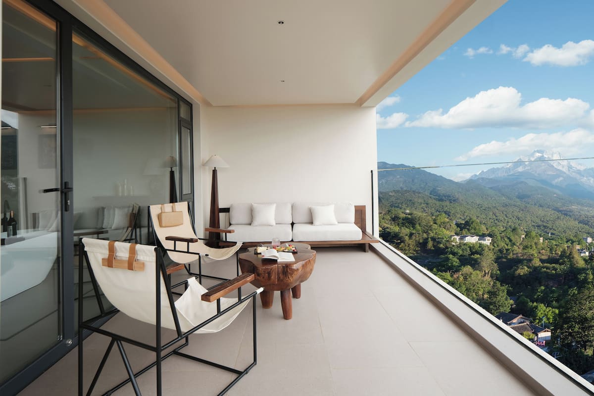 Un balcón con un sofá blanco, una silla de madera y una mesita.