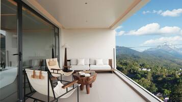 Un balcón con sofá, una silla y una mesa, con vistas a un paisaje montañoso.