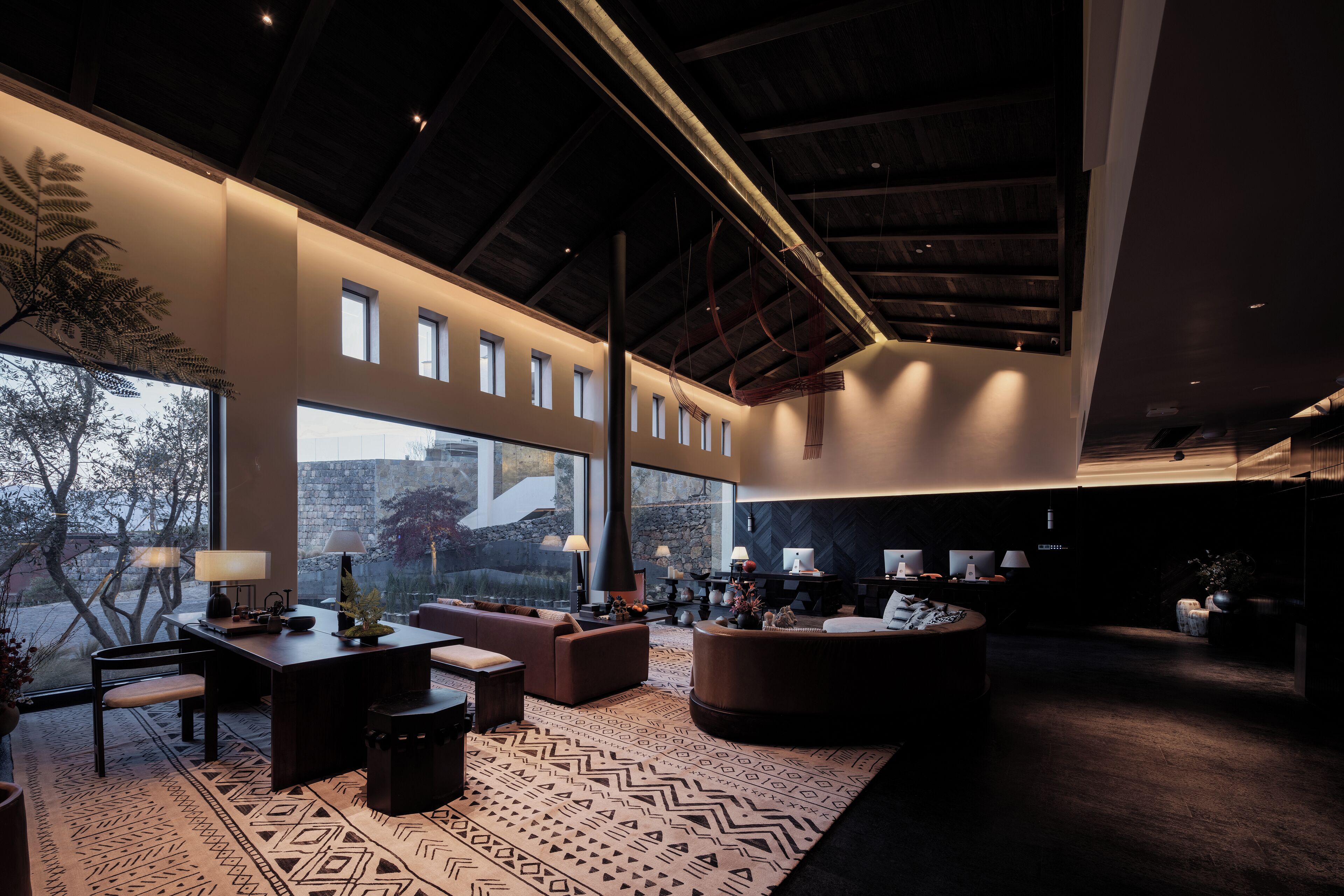 A spacious living area with a high ceiling, large windows, and modern furniture.