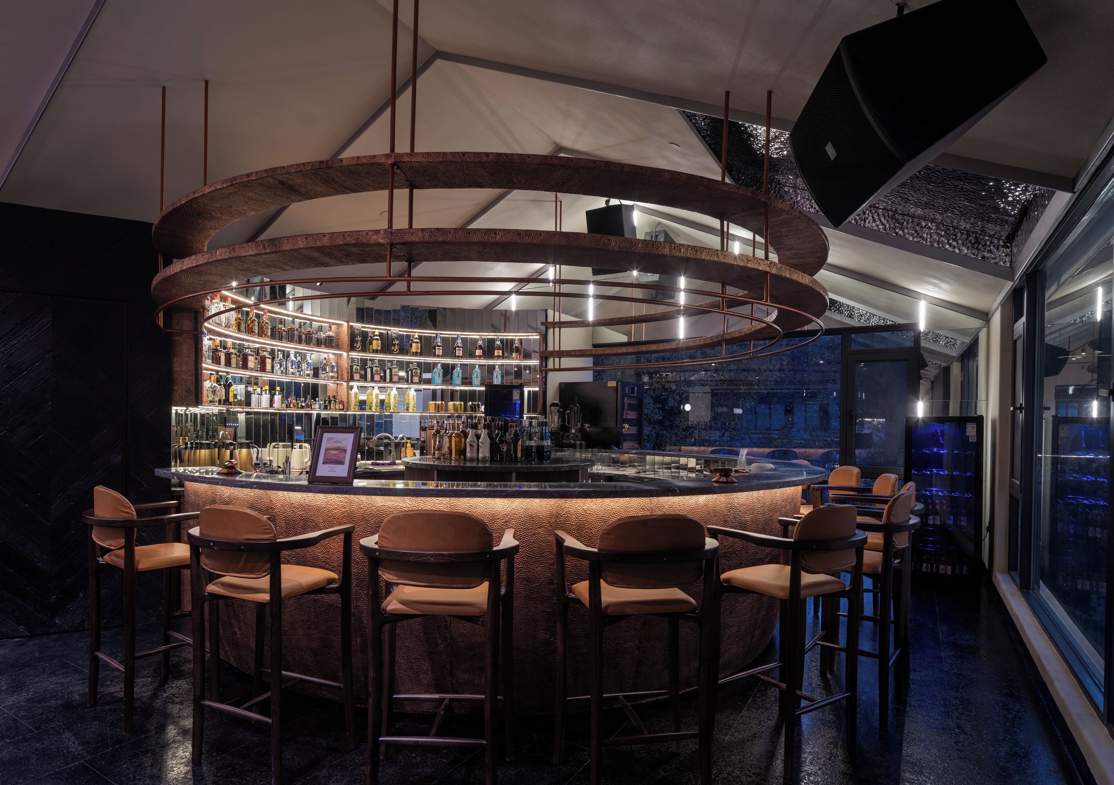 Uma área de bar com balcão circular, diversas opções de assento e interior bem iluminado.