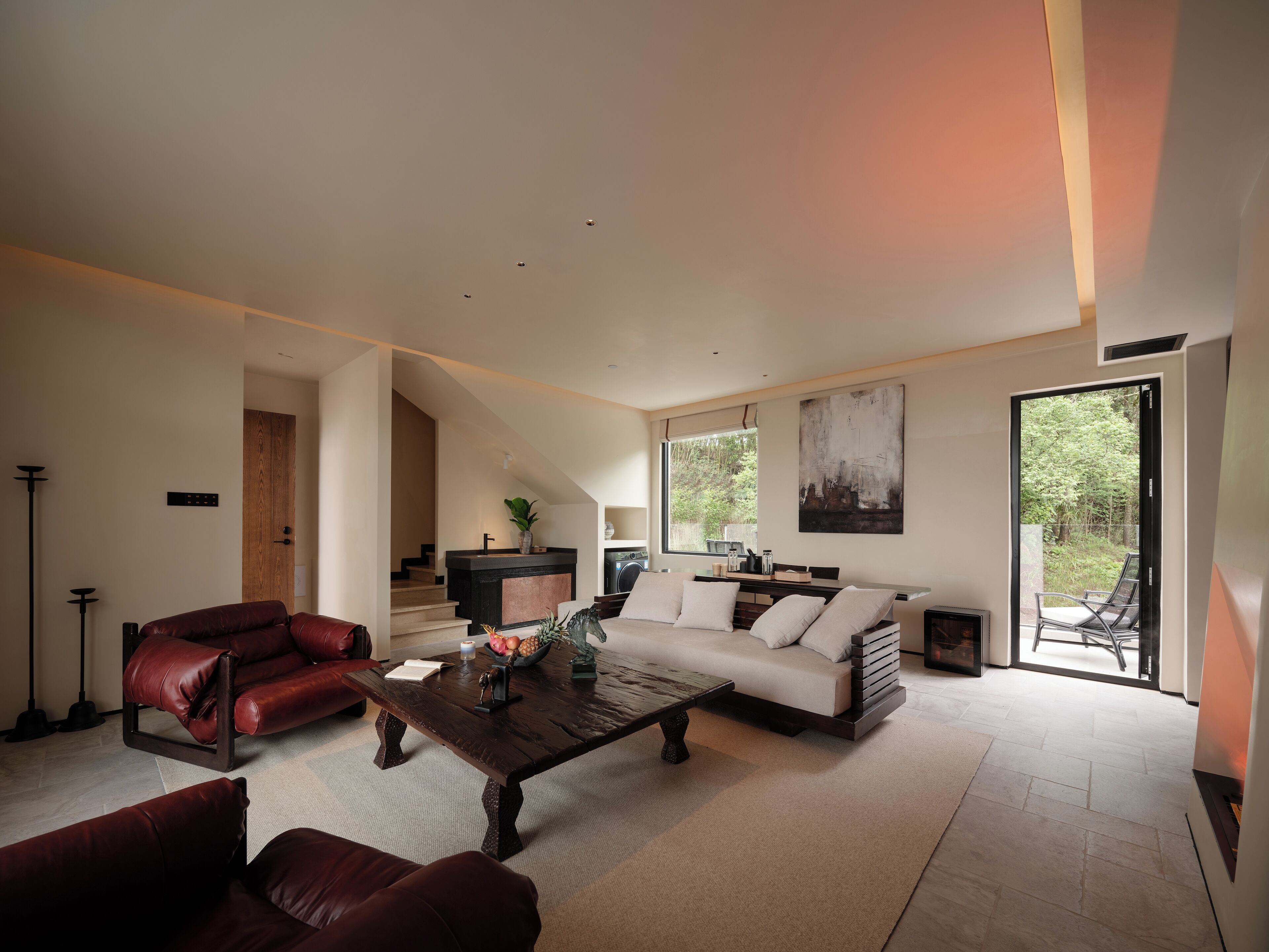 A modern living room with a sofa, two armchairs, a coffee table, and a staircase leading to a kitchen.