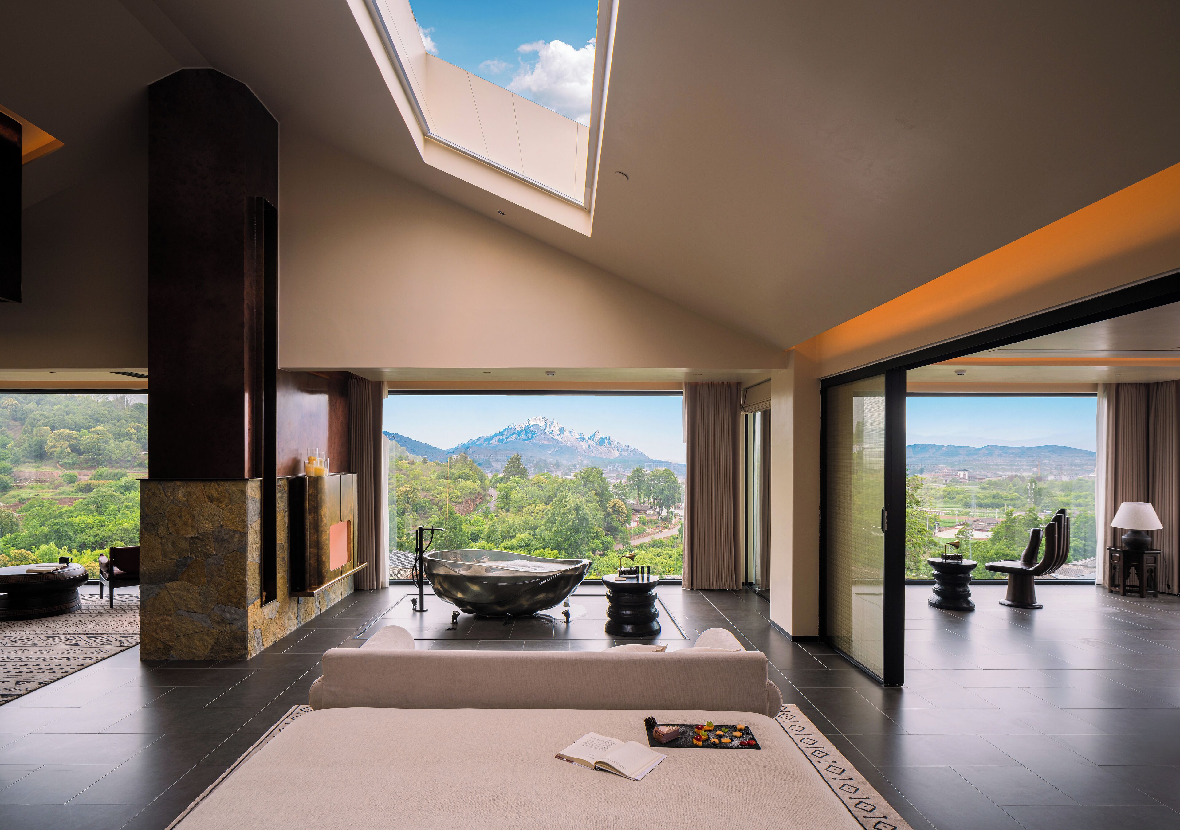 Un interior moderno con un tragaluz grande, una chimenea de piedra y vistas a un paisaje montañoso.