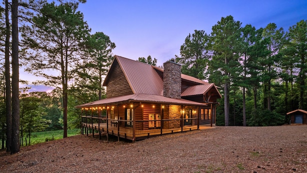 A log cabin with a stone chimney, wooden deck, and string lights.