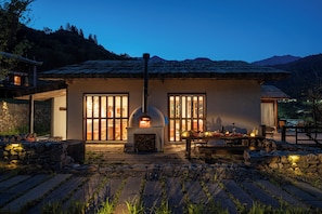 Una casa rústica con chimenea de piedra, ventanas amplias y un comedor con mesas al aire libre.