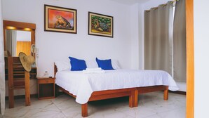 Un dormitorio con una cama de madera, ropa de cama blanca, una mesita de noche de madera, una silla, un espejo y dos cuadros en la pared.