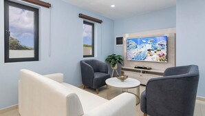 A modern living room with a flat-screen TV, two grey armchairs, a white sofa, and a small round table.
