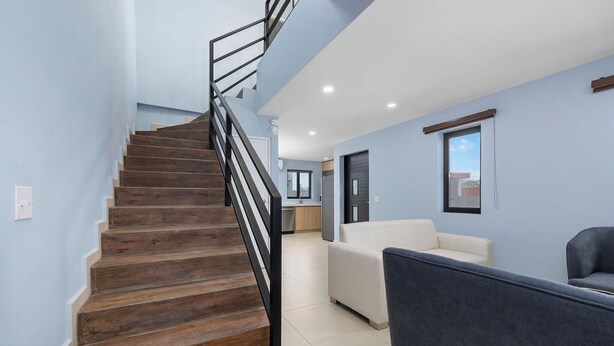 A staircase with wooden steps and black railings leading to a living area with a sofa and a chair.