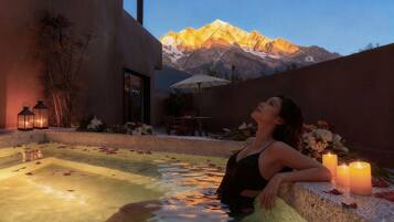 A woman relaxing in a hot tub with a mountain view, surrounded by candles and flowers.