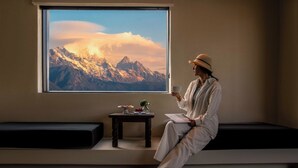 A person sitting on a bench in a room with a large window displaying a mountain view. - Mucheng Xichi Snow Mountain Art Resort (Lijiang)