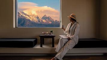 A person sitting on a bench in a room with a large window displaying a mountain view.
