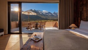 A hotel room with a bed, a wooden desk with a book, a lamp, and a view of mountains through a glass door. - Mucheng Xichi Snow Mountain Art Resort (Lijiang)
