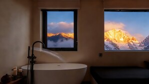 A bathroom with a large bathtub, a window with a mountain view, and a small bedside table with candles. - Mucheng Xichi Snow Mountain Art Resort (Lijiang)