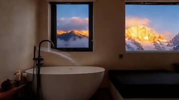 A bathroom with a large bathtub, a window with a mountain view, and a small bedside table with candles.