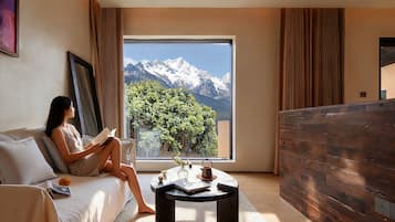 A modern hotel room with a large window offering a mountain view, a cozy sitting area with a coffee table, and a wooden accent wall.