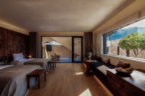 Ett modernt hotellrum med två sängar, en sittgrupp med utsikt och ett matbord med frukt.