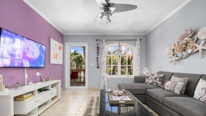 Una sala de estar con televisor, sofá, mesa de centro y balcón con vista a palmeras.